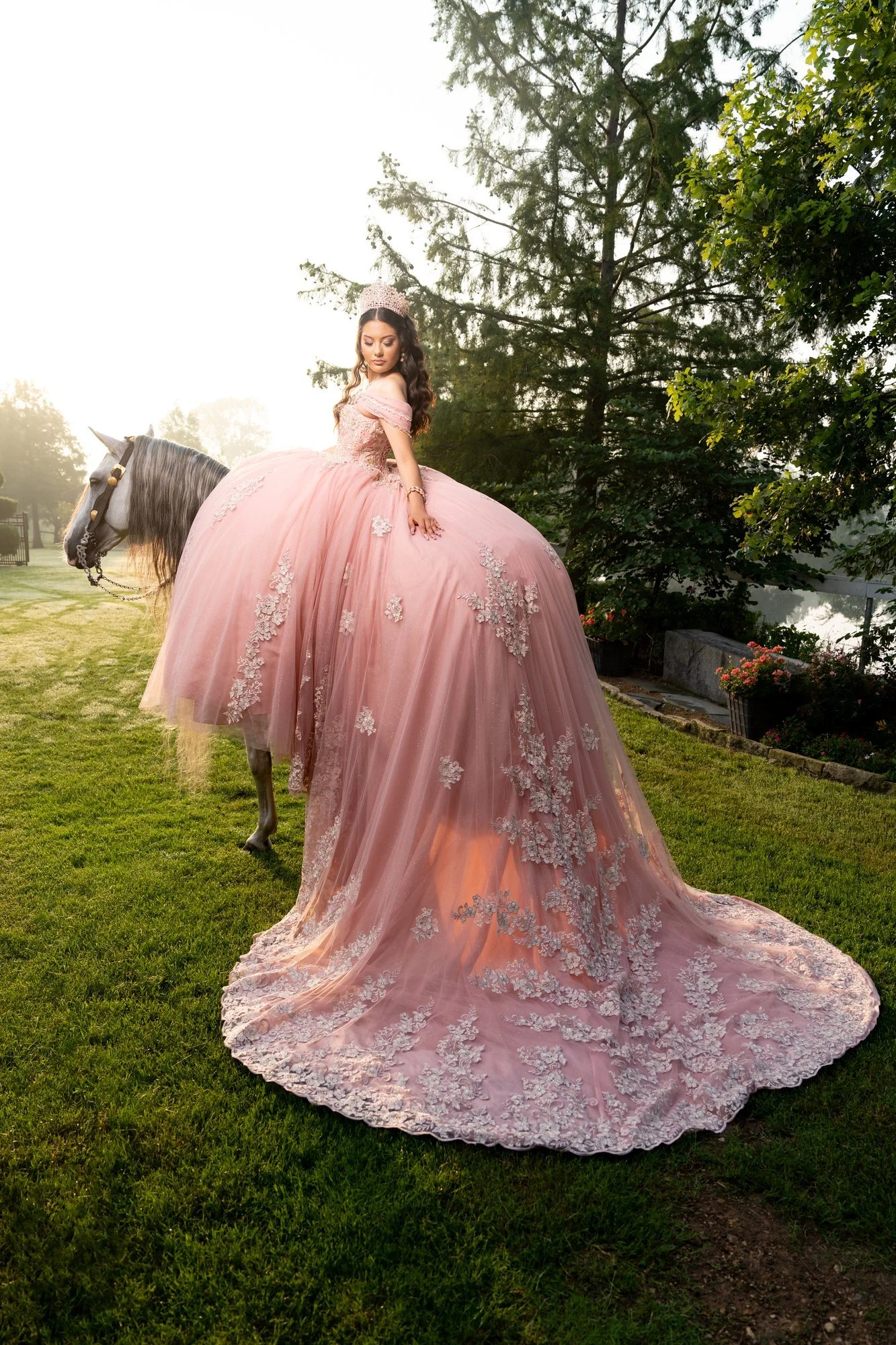 Quinceañera con vestido rosa y la cola extendida junto a un caballo