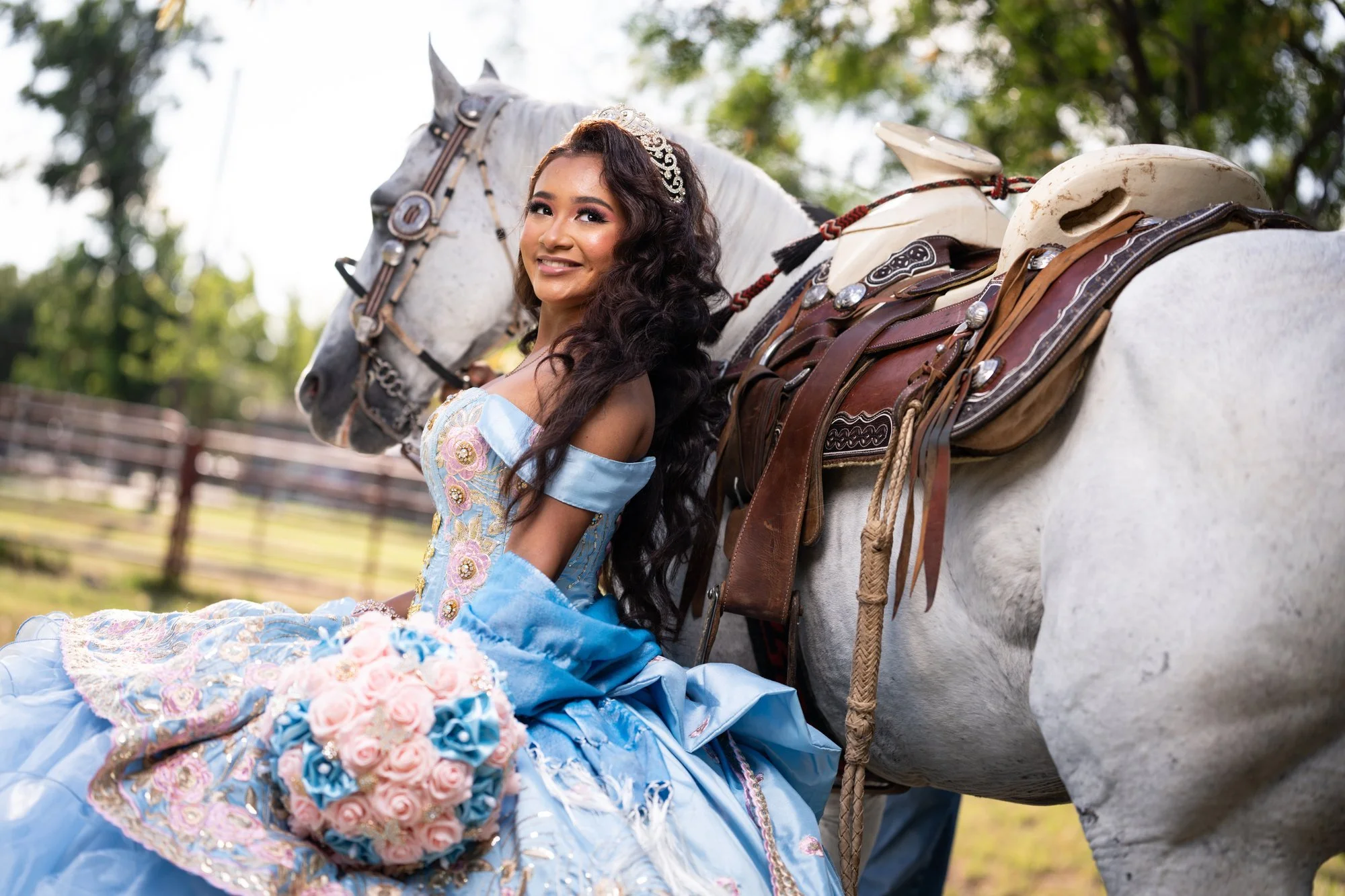 Quinceañera con vestido charro azul junto a un caballo blanco