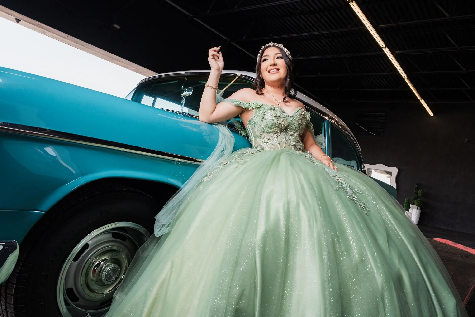 Quinceañera con vestido verde junto a un auto clásico turquesa