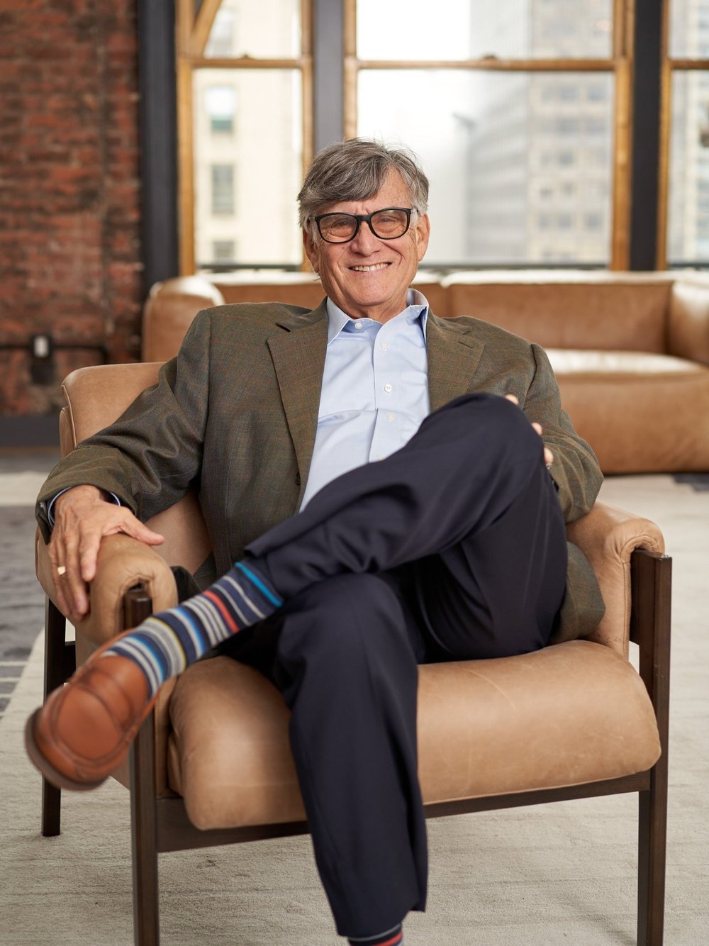 Seated environmental portrait of a board member in a brick-walled New York office