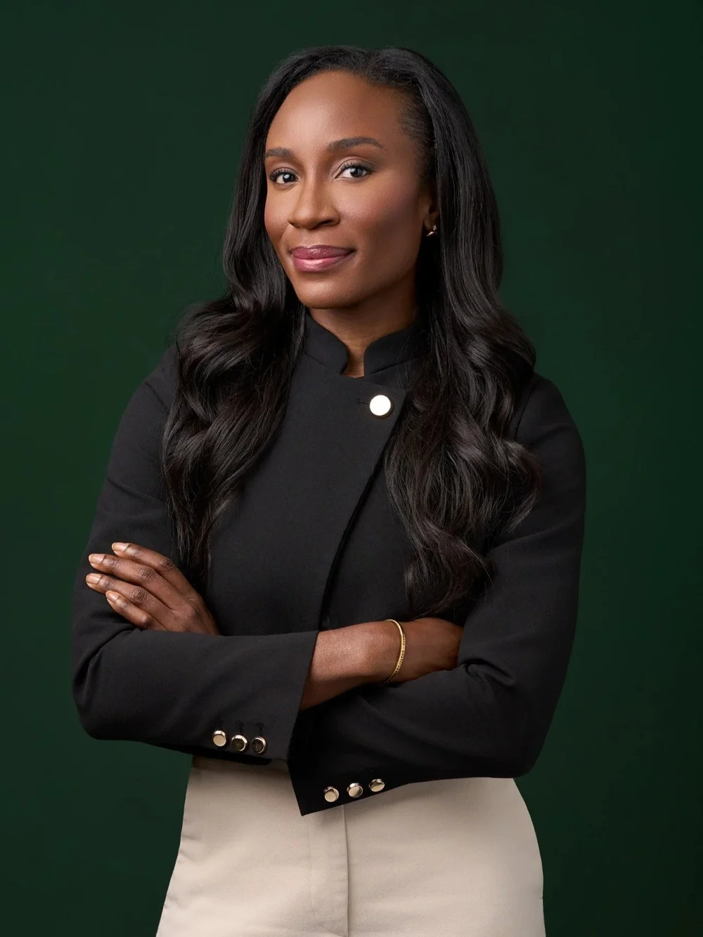 Executive headshot of a woman in a black jacket with folded arms against a deep green studio background