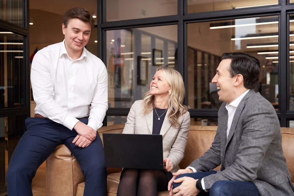 Three colleagues talking around a laptop during a relaxed meeting in a modern office