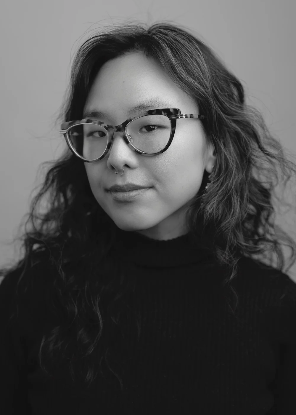 Black-and-white studio portrait of a woman wearing cat-eye glasses and a dark turtleneck