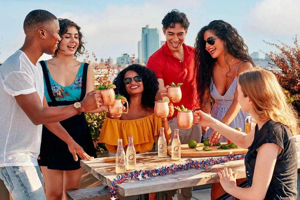 Rooftop lifestyle photograph of friends raising copper mugs around a table for Q Mixers