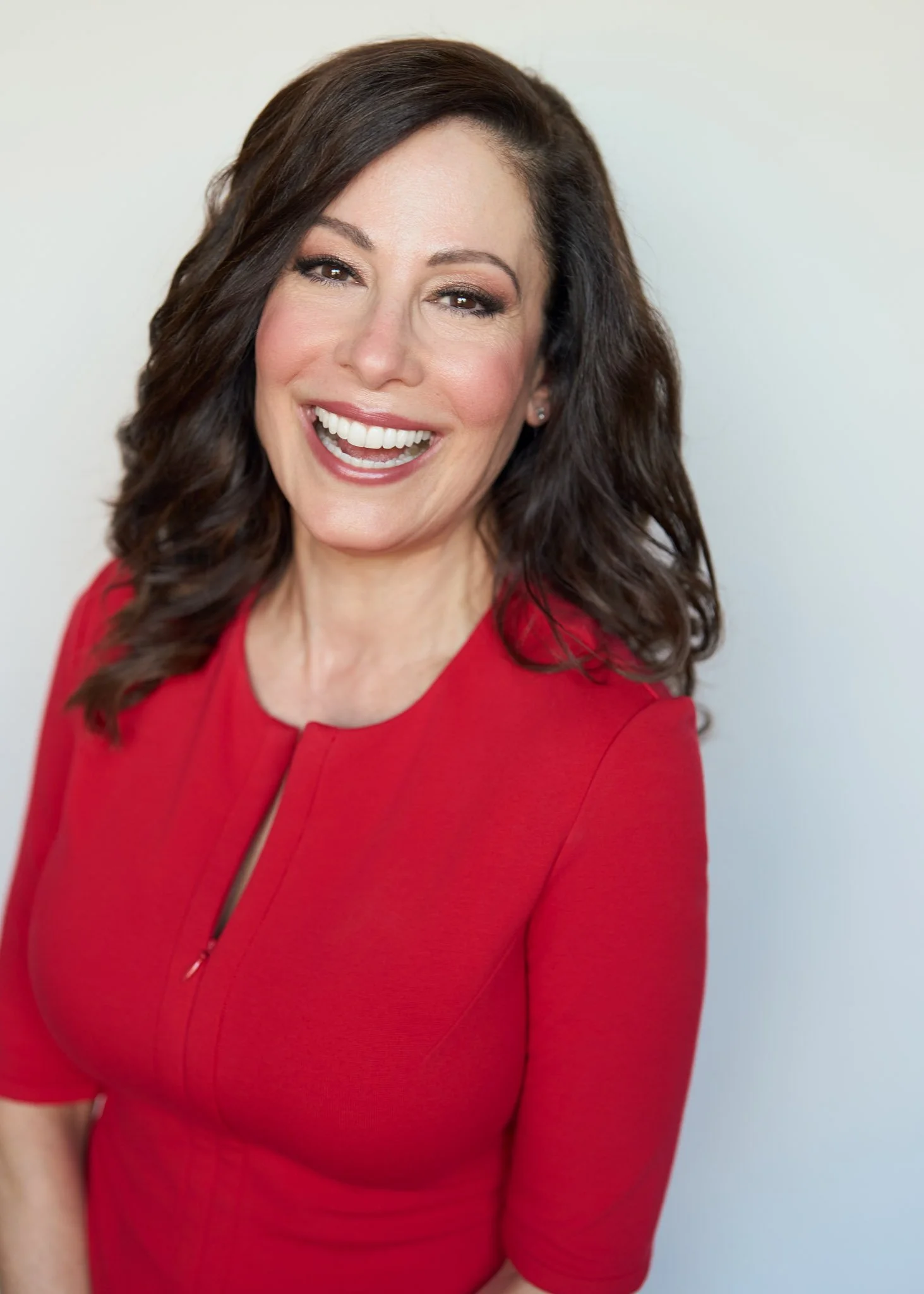 Actor headshot of a brunette woman in a red dress laughing against a white background, New York City