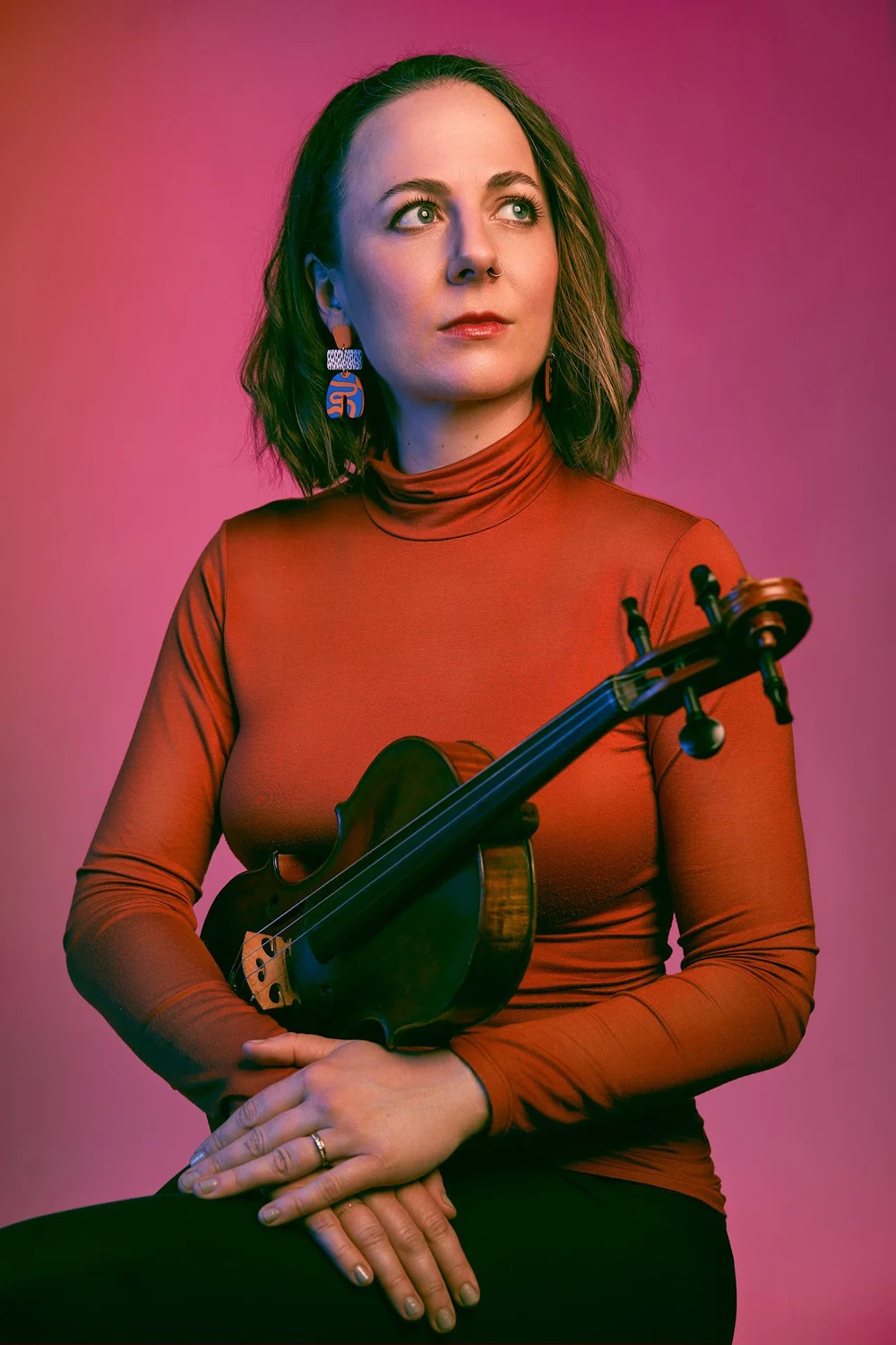 Editorial studio portrait of a violinist holding her instrument under pink and green lighting