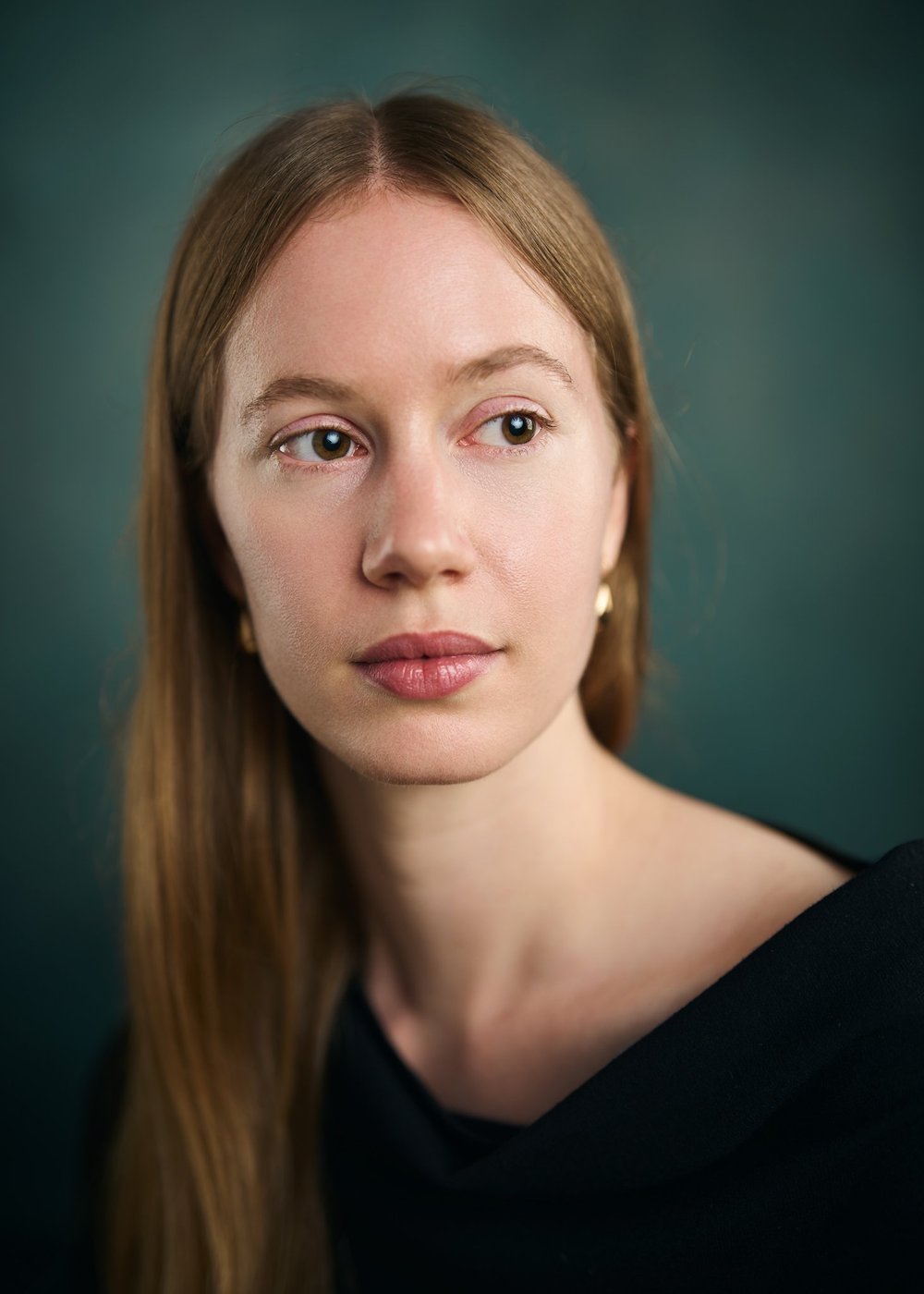 Theatrical actor headshot of a woman looking off camera against a dark green studio background