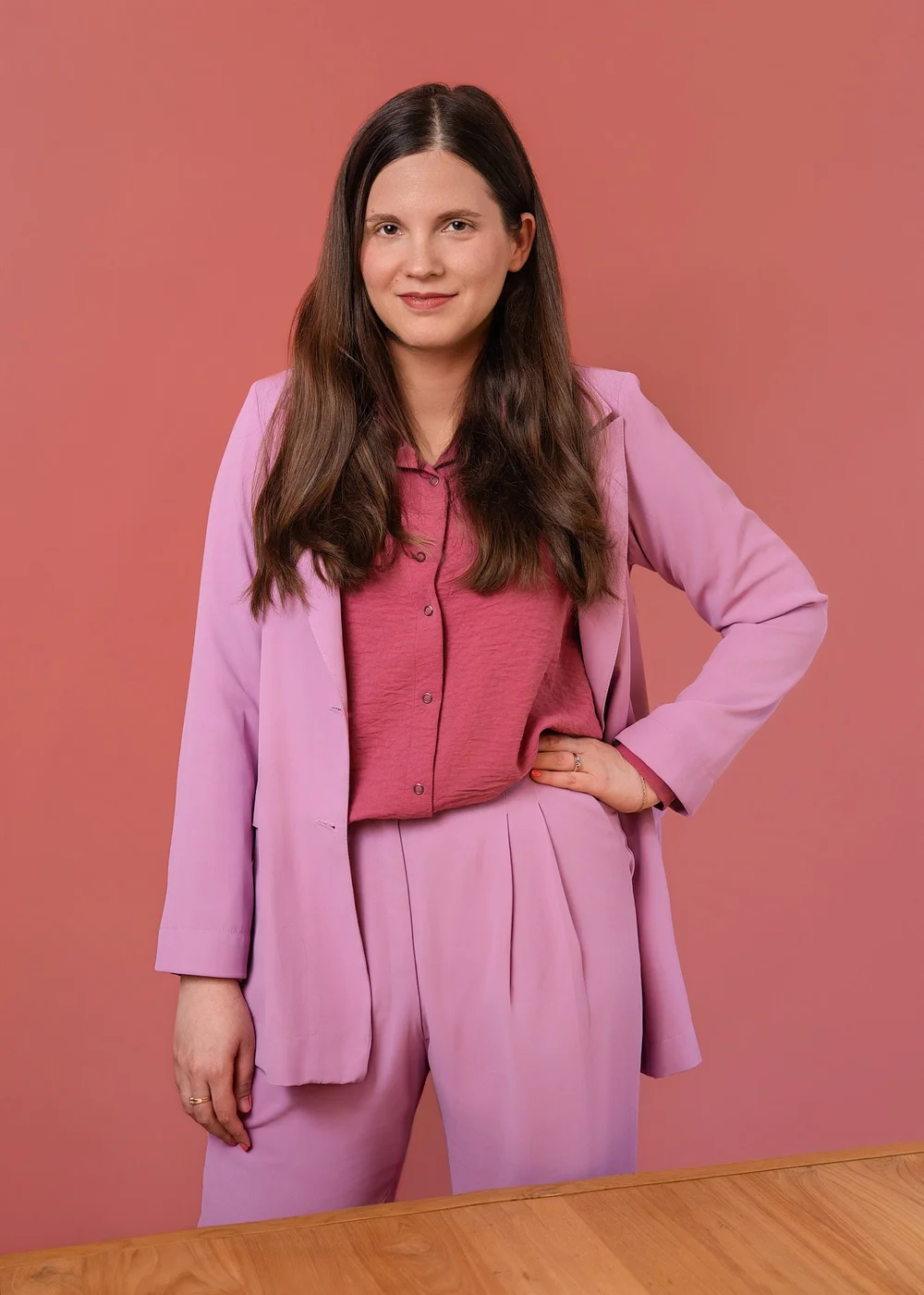 Full-length editorial portrait of a woman in a pink suit standing against a coral background