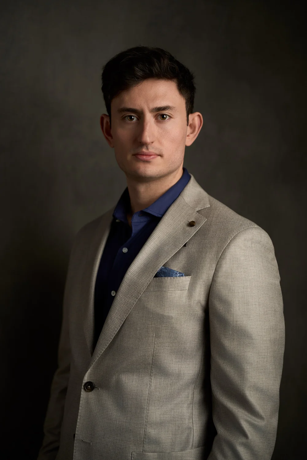 Studio executive portrait of a man in a light jacket against a textured charcoal background