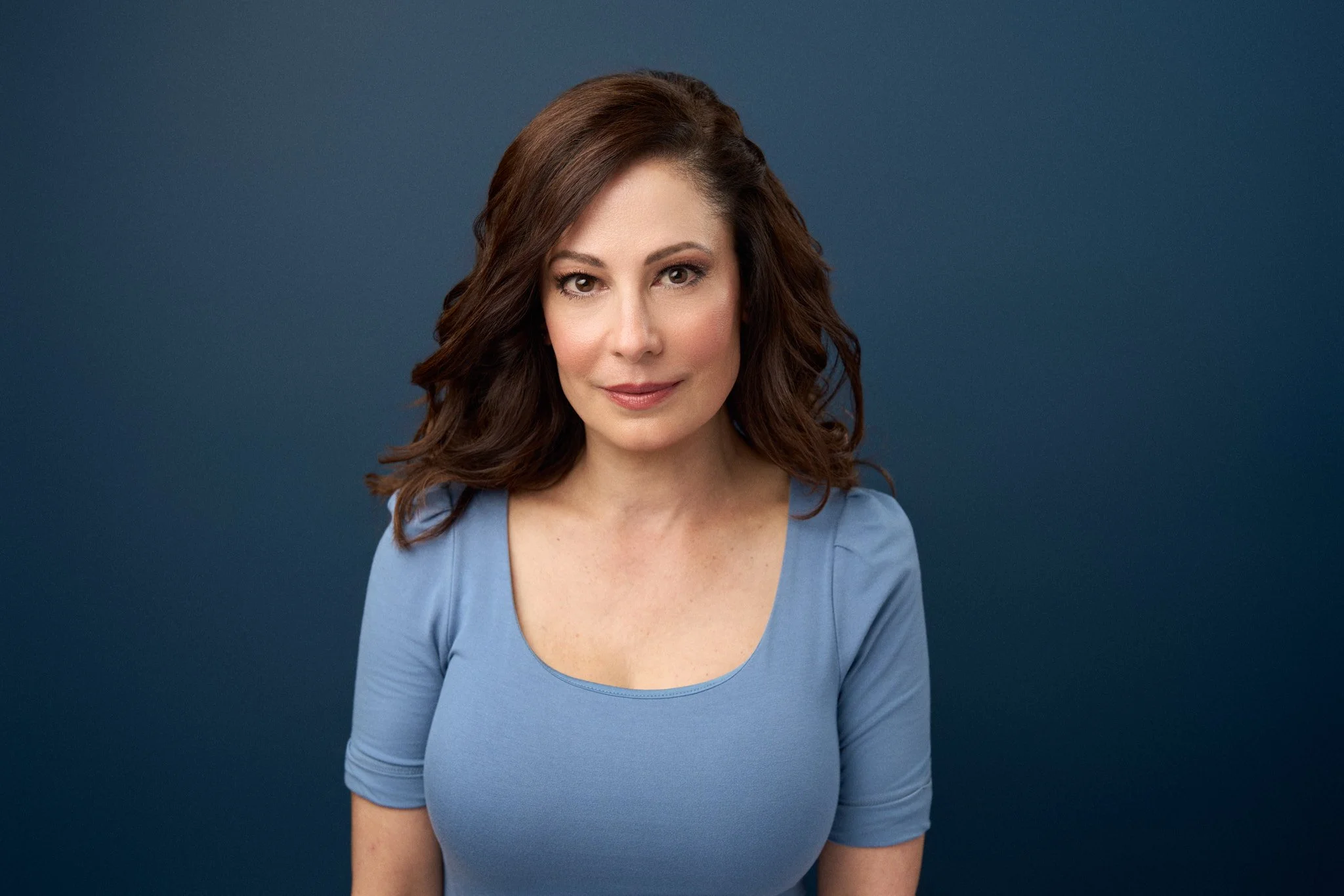 Actor headshot of a brunette woman in a light blue top against a deep navy backdrop, New York City