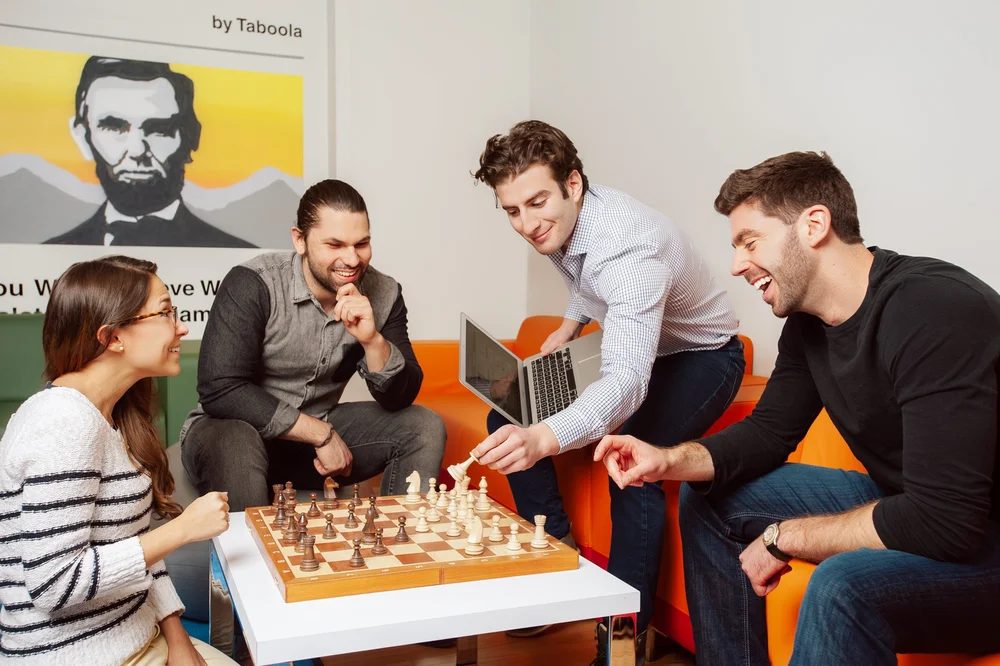 Corporate lifestyle photograph of four colleagues gathered around a chessboard in an office