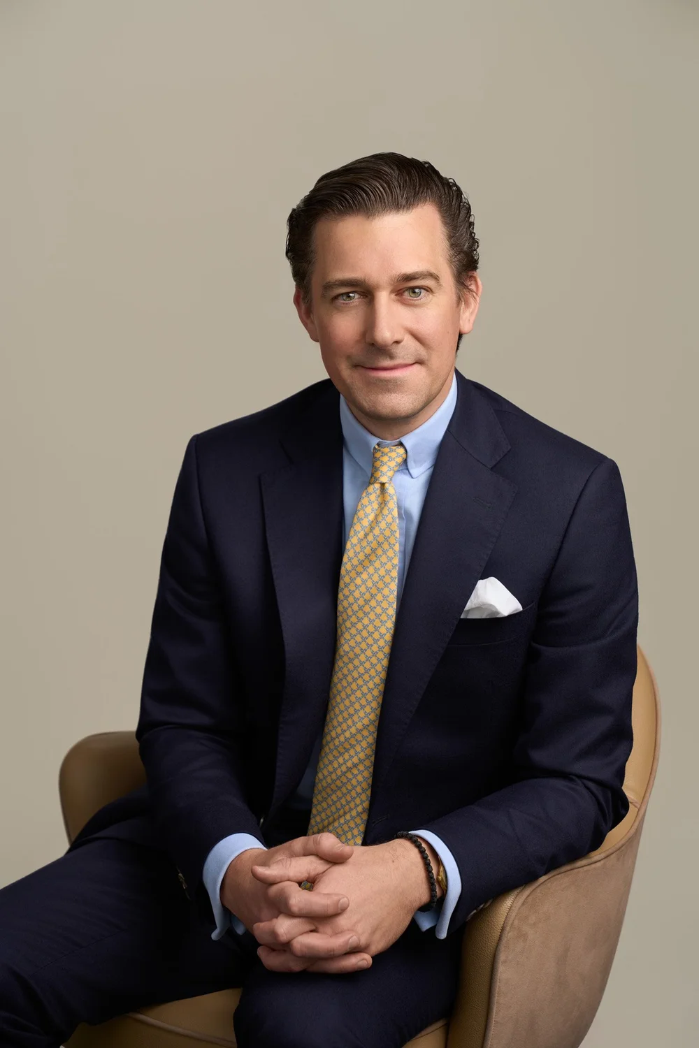 Seated lawyer portrait in a navy suit and gold tie against a warm neutral studio background