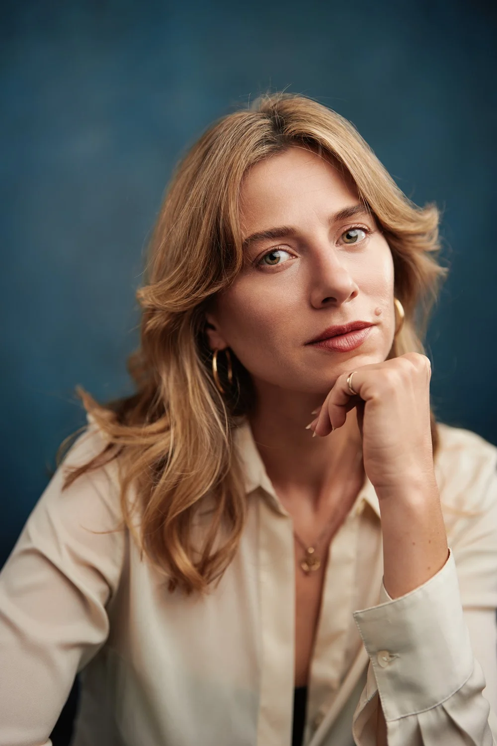 Close actor headshot of a woman against a deep blue background with her hand resting beneath her chin
