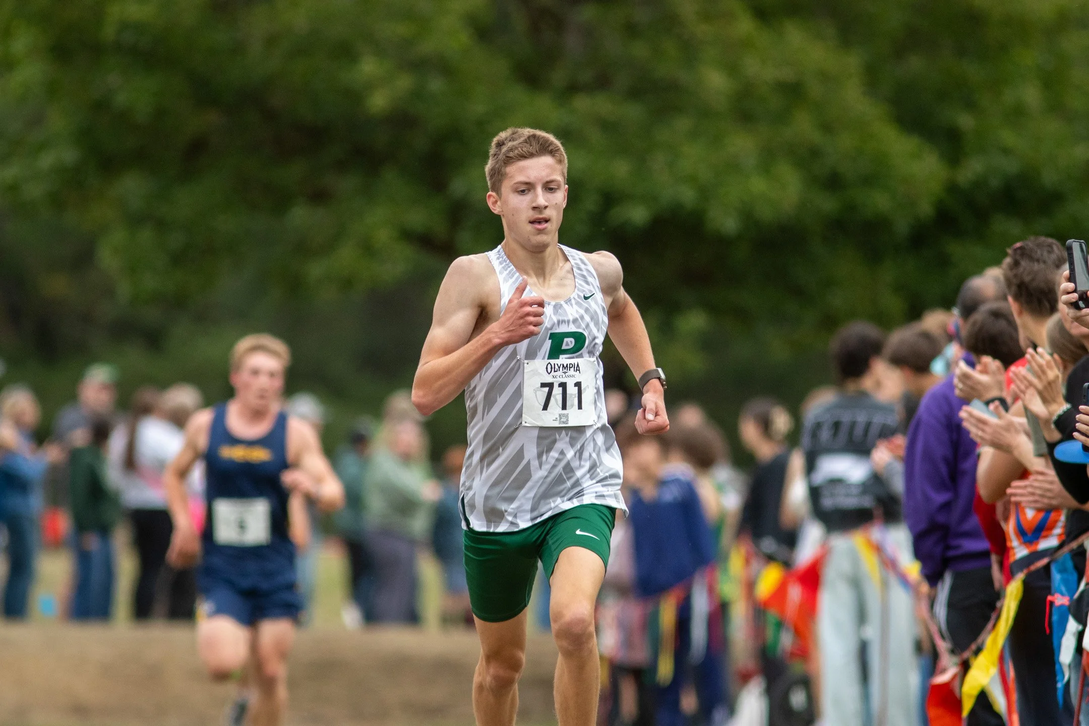 Boy in white and green Peninsula jersey, bib 711, leading the junior boys' race at the 2026 Olympia XC Classic.