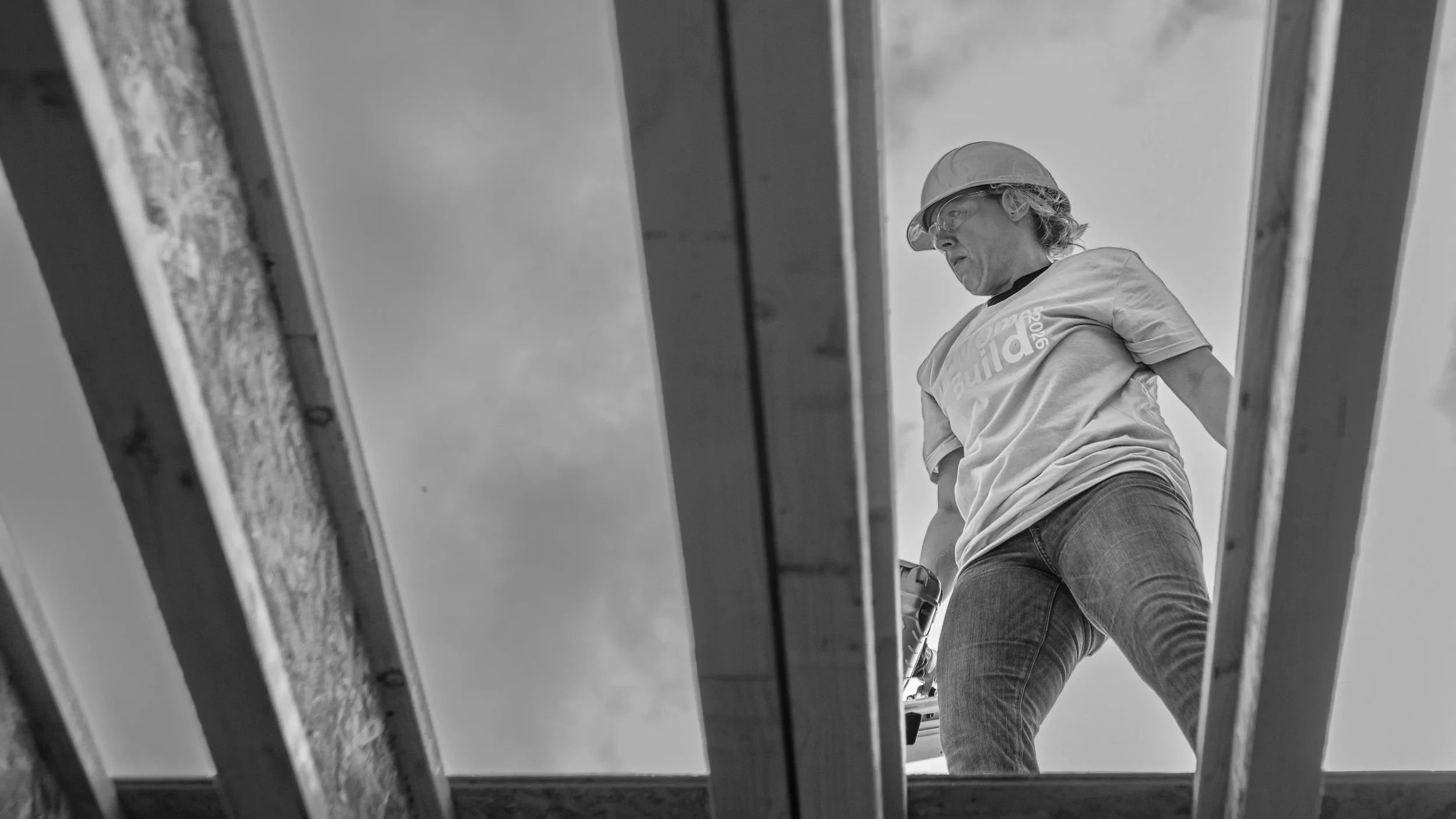 Volunteer framing a roof seen from below through open joists, Habitat Women Build 2026