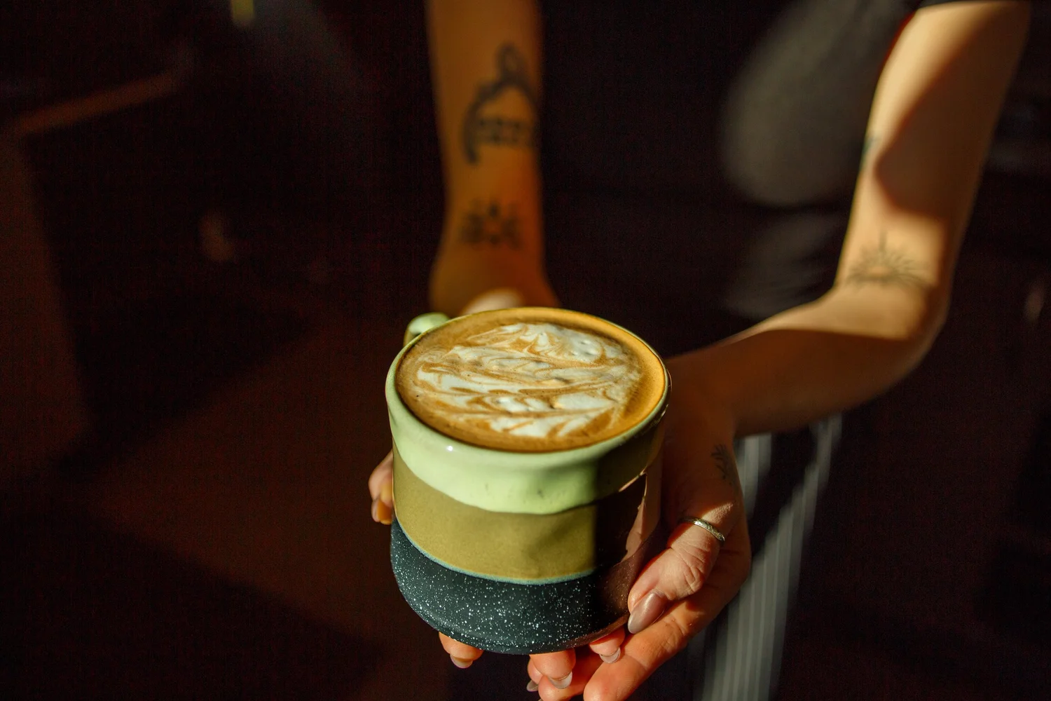 Hand holding a latte with foam art in a green ceramic mug at Taylor Ray's Cafe in Olympia