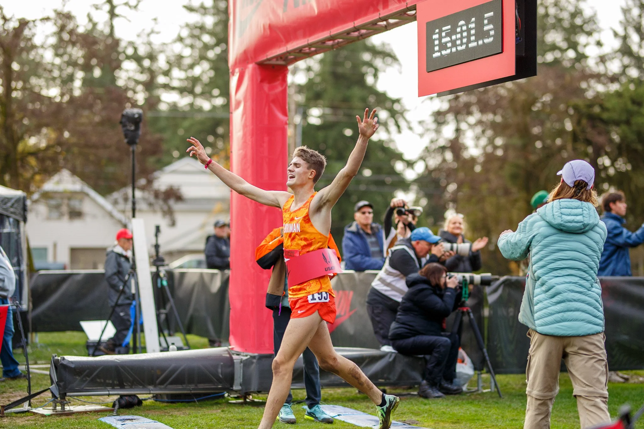A male high school cross country runner breaking the red Nike finish line tape at the 2025 Nike Cross Nationals (NXN) championship in Portland, Oregon.