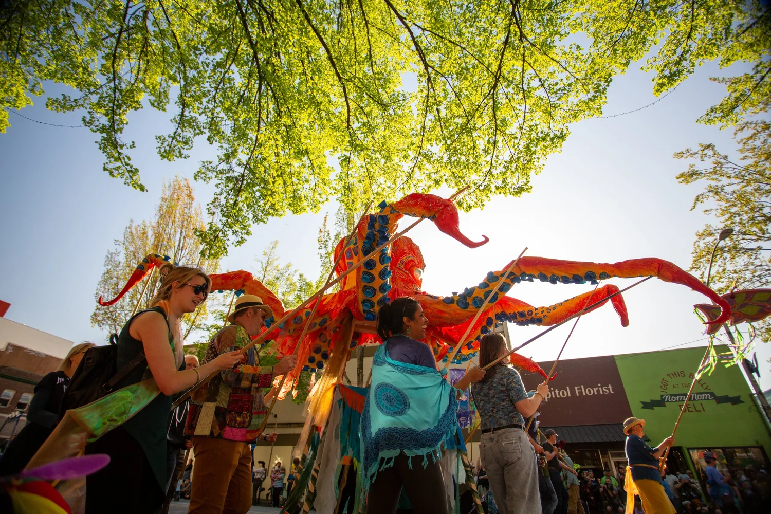 Giant red octopus puppet carried through downtown Olympia during the Procession of the Species, sunlight through the trees