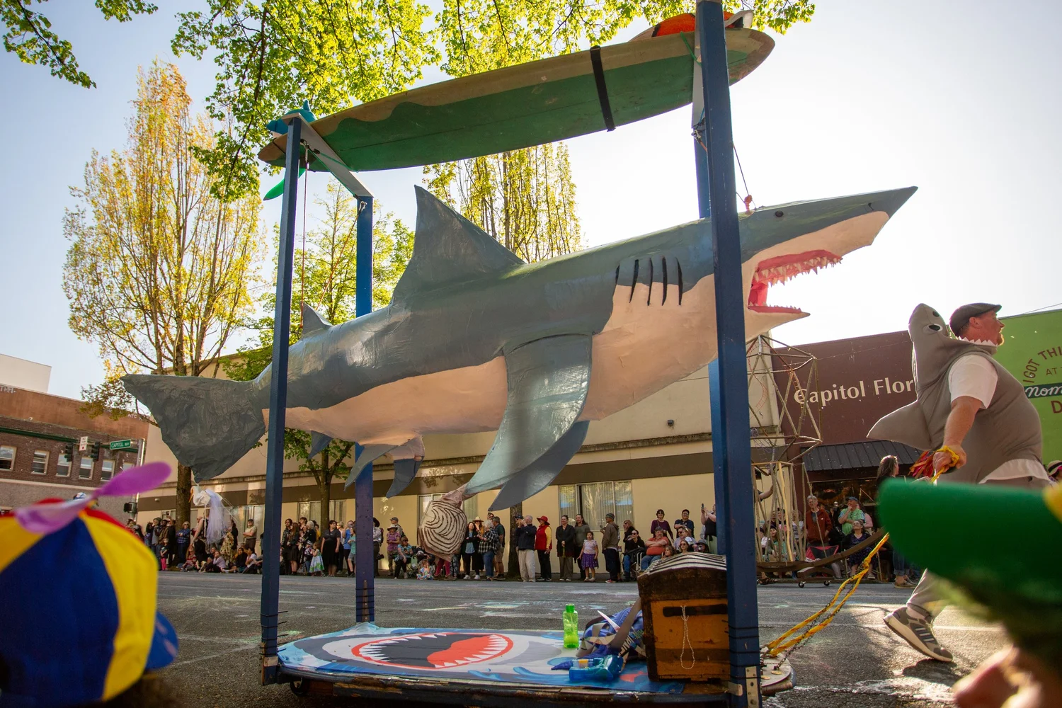 Large shark puppet above a street lined with spectators at the Procession of the Species in Olympia