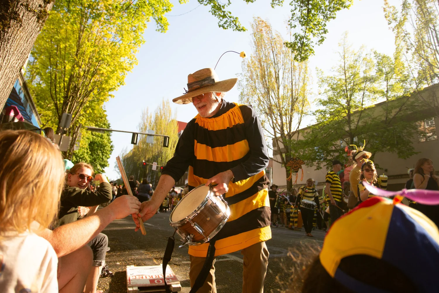 Performer in a striped bee costume reaches toward a spectator in the crowd at the Procession of the Species in Olympia