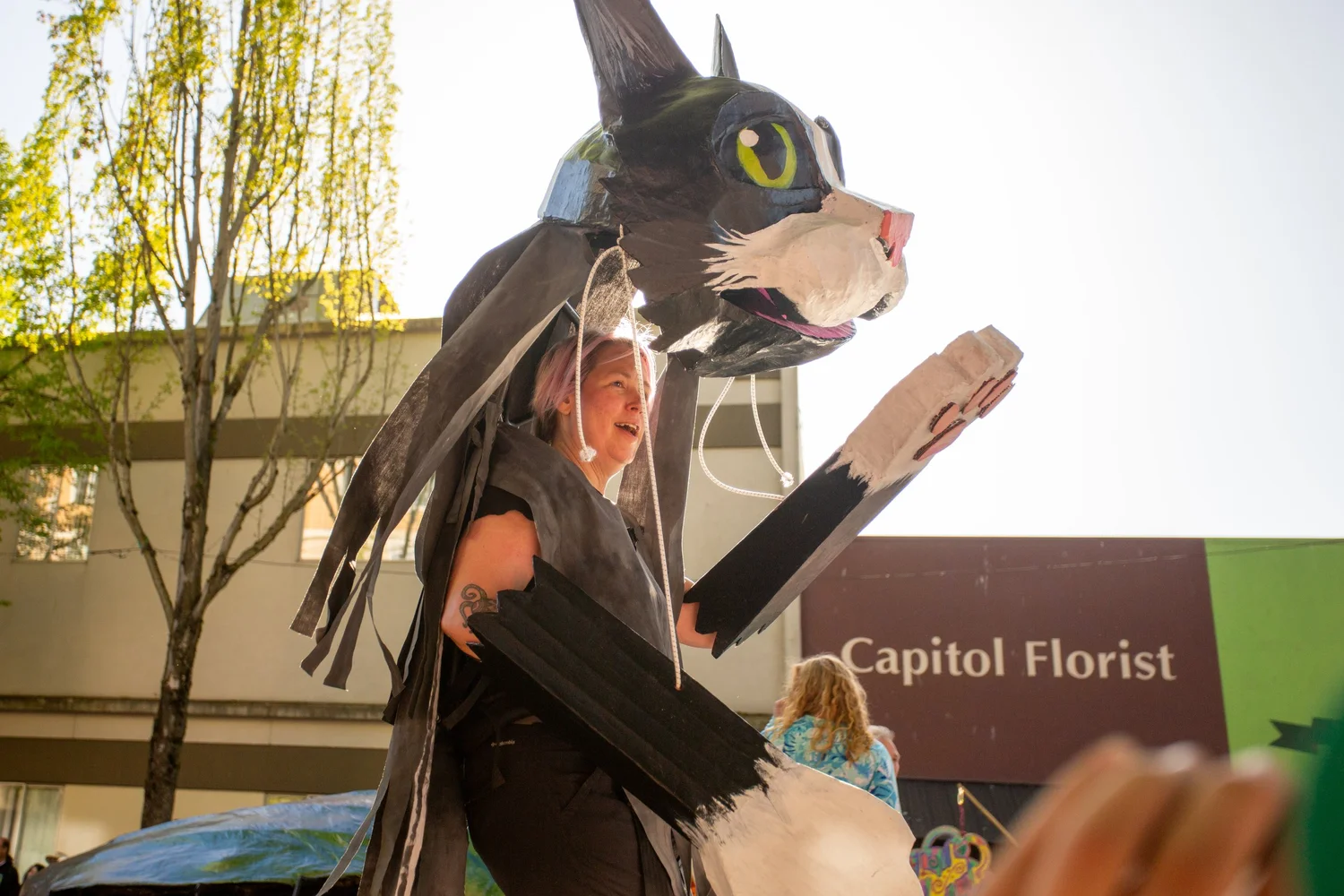 Performer carrying a black cat puppet past Capitol Florist at the Procession of the Species in Olympia