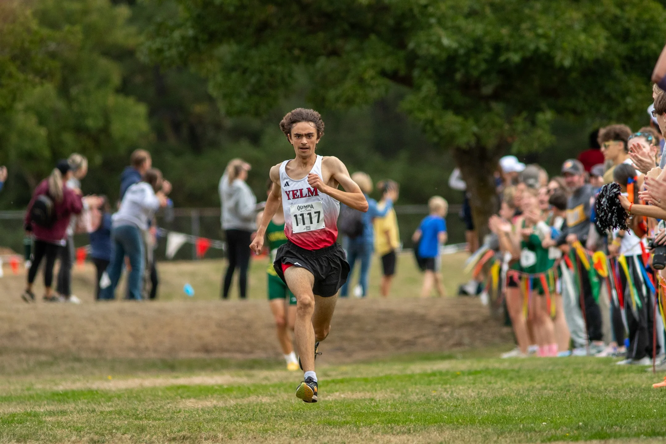Boy in white and red Yelm jersey, bib 1117, running toward the finish at the 2026 Olympia XC Classic.