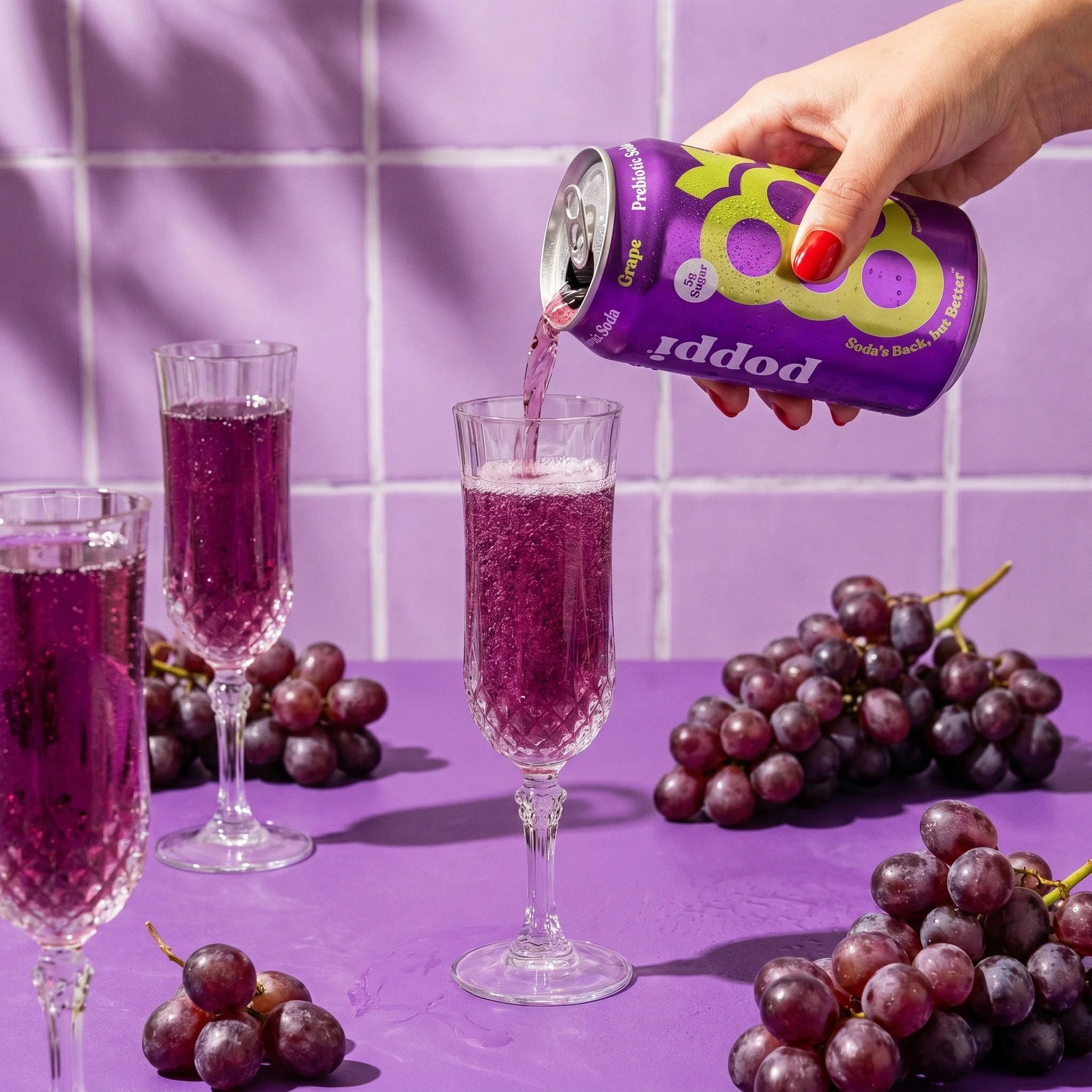 Styled photograph of a grape soda can being poured into champagne flutes