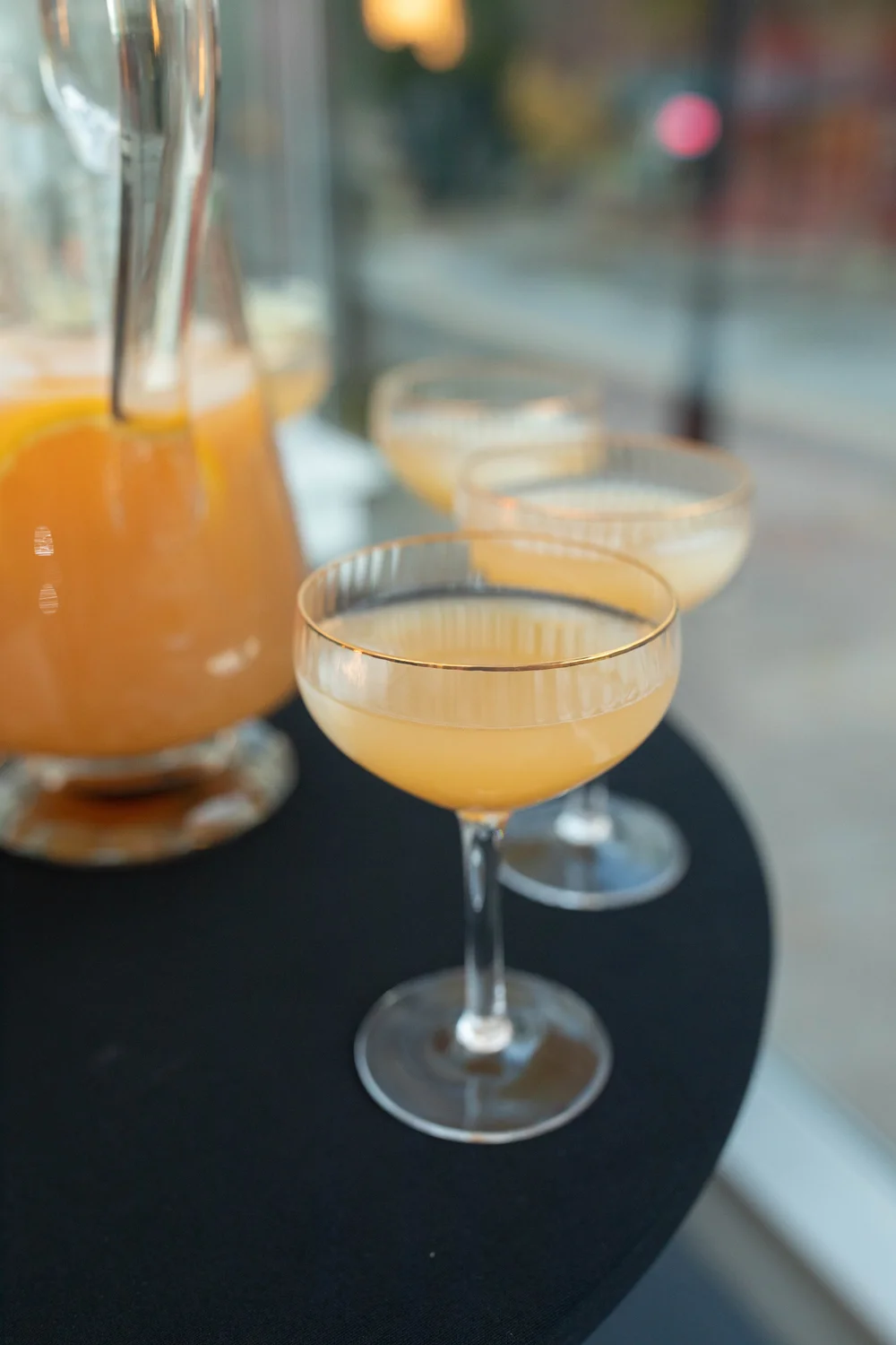 A golden drink served in a coupe beside a glass pitcher. Photograph by Kuffel Photography.