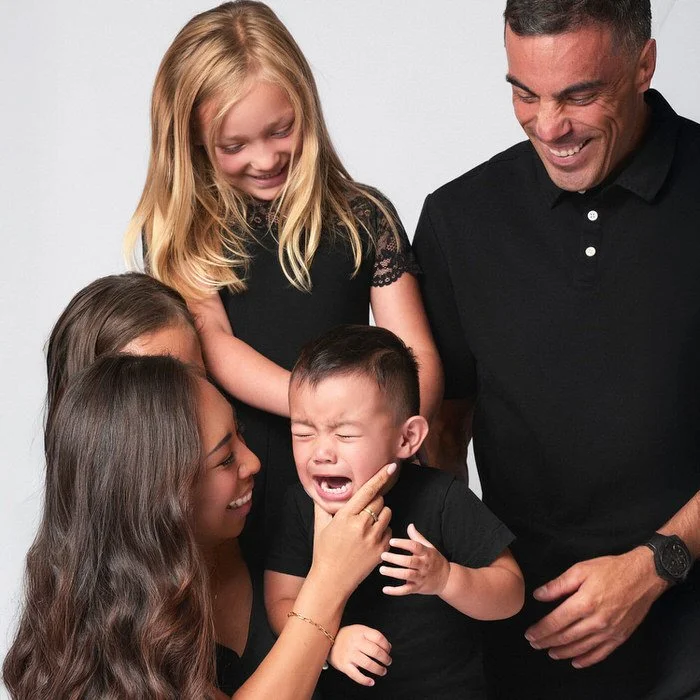 Studio family portrait — family of five in all black sharing a candid moment of laughter