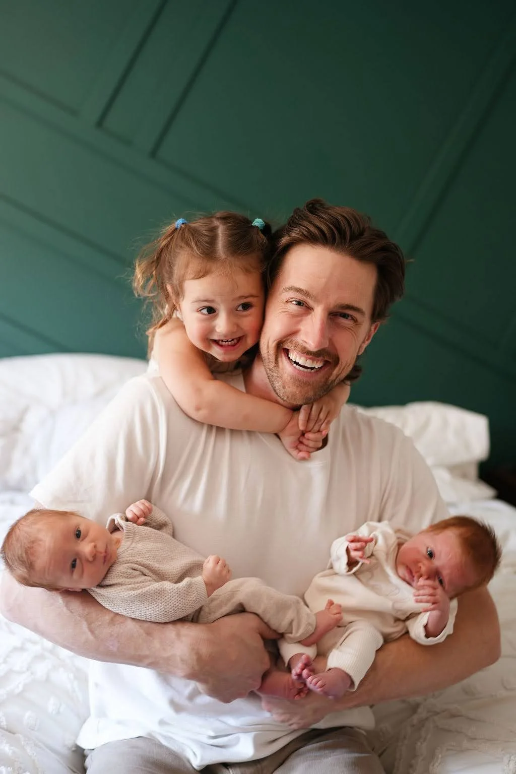 Mark Eadie holding his newborn twins with his toddler daughter around his shoulders