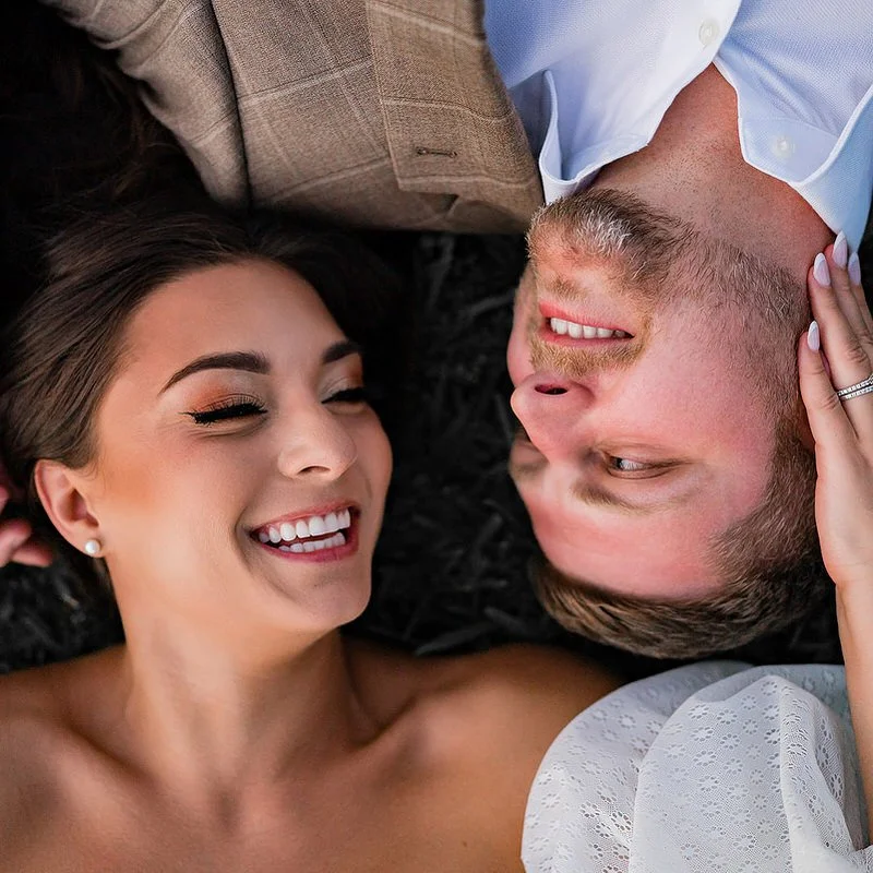 Outdoor wedding portrait — couple lying on grass smiling, groom upside down