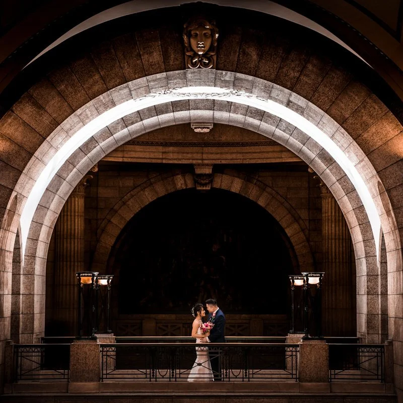 Wedding portrait — couple under a stone arch with dramatic lighting
