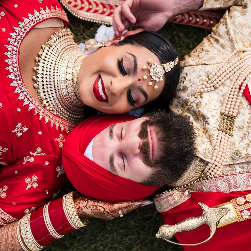 Punjabi wedding portrait — couple smiling and lying in the grass outdoors