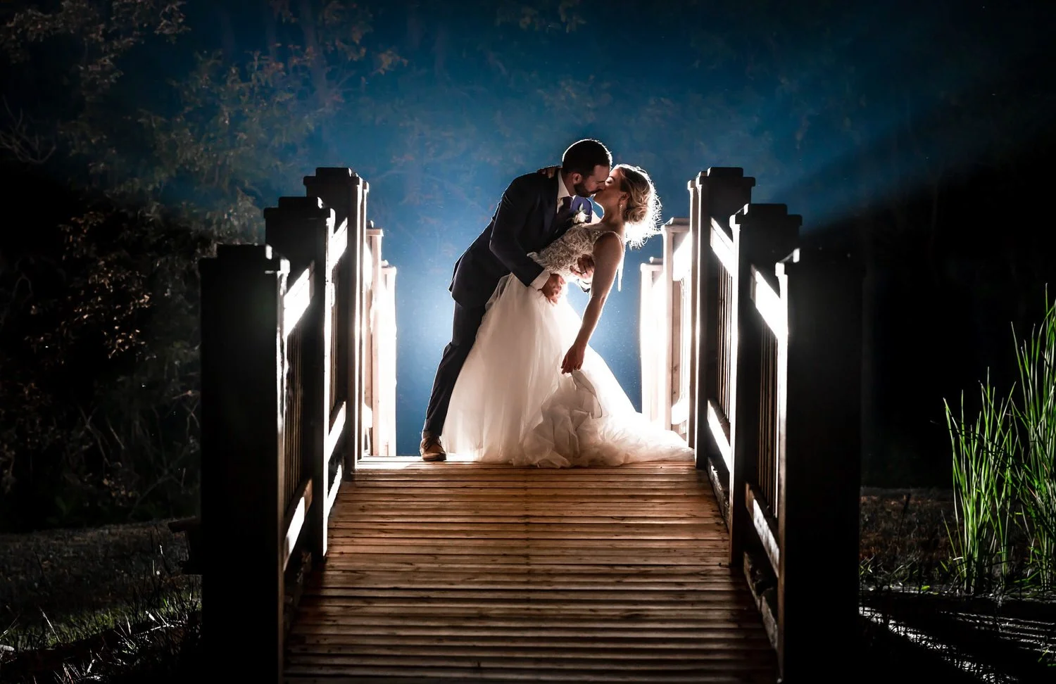 Winnipeg wedding photography — couple sharing a dramatic dip kiss on a bridge, backlit by golden light