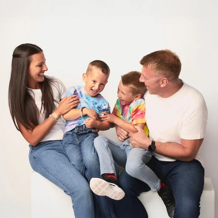 Studio family portrait — family of four in tie-dye shirts and jeans laughing together