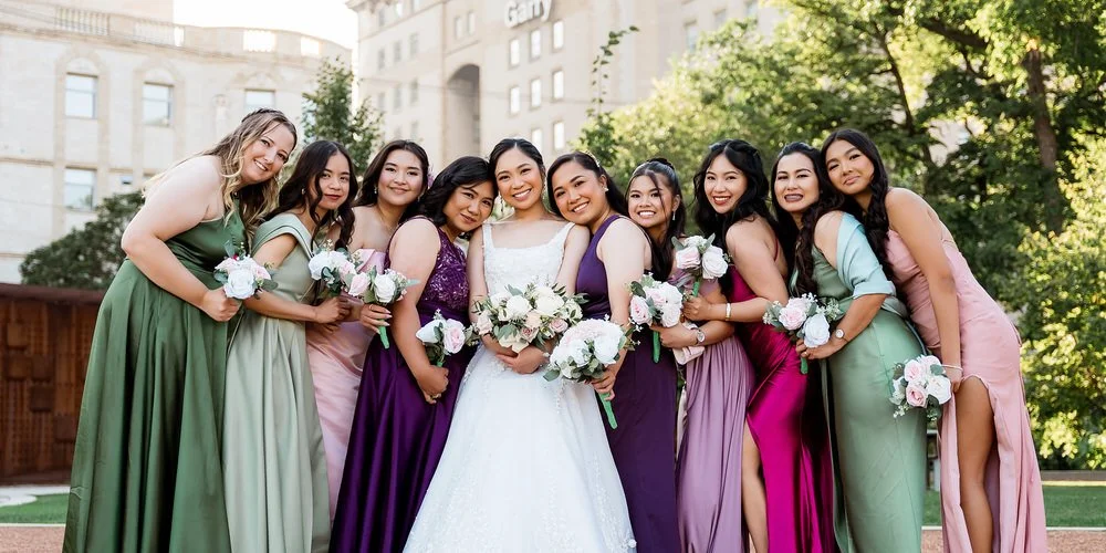 Outdoor wedding — bridal party women smiling in a garden with skyline in the background
