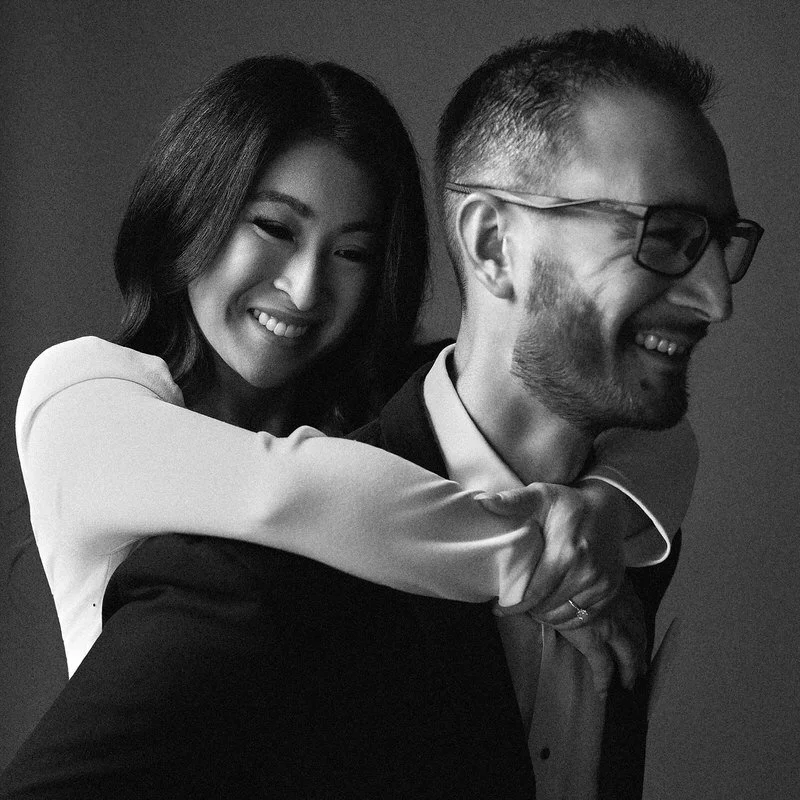 Studio wedding portrait — couple laughing during a piggyback pose, black and white