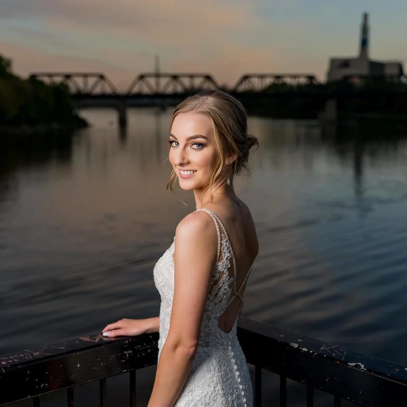 Outdoor bridal portrait — bride posing in flattering light with a river bridge in the background