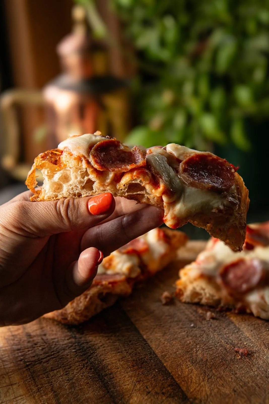 A hand holding a slice of salami pinsa with an open, airy crumb