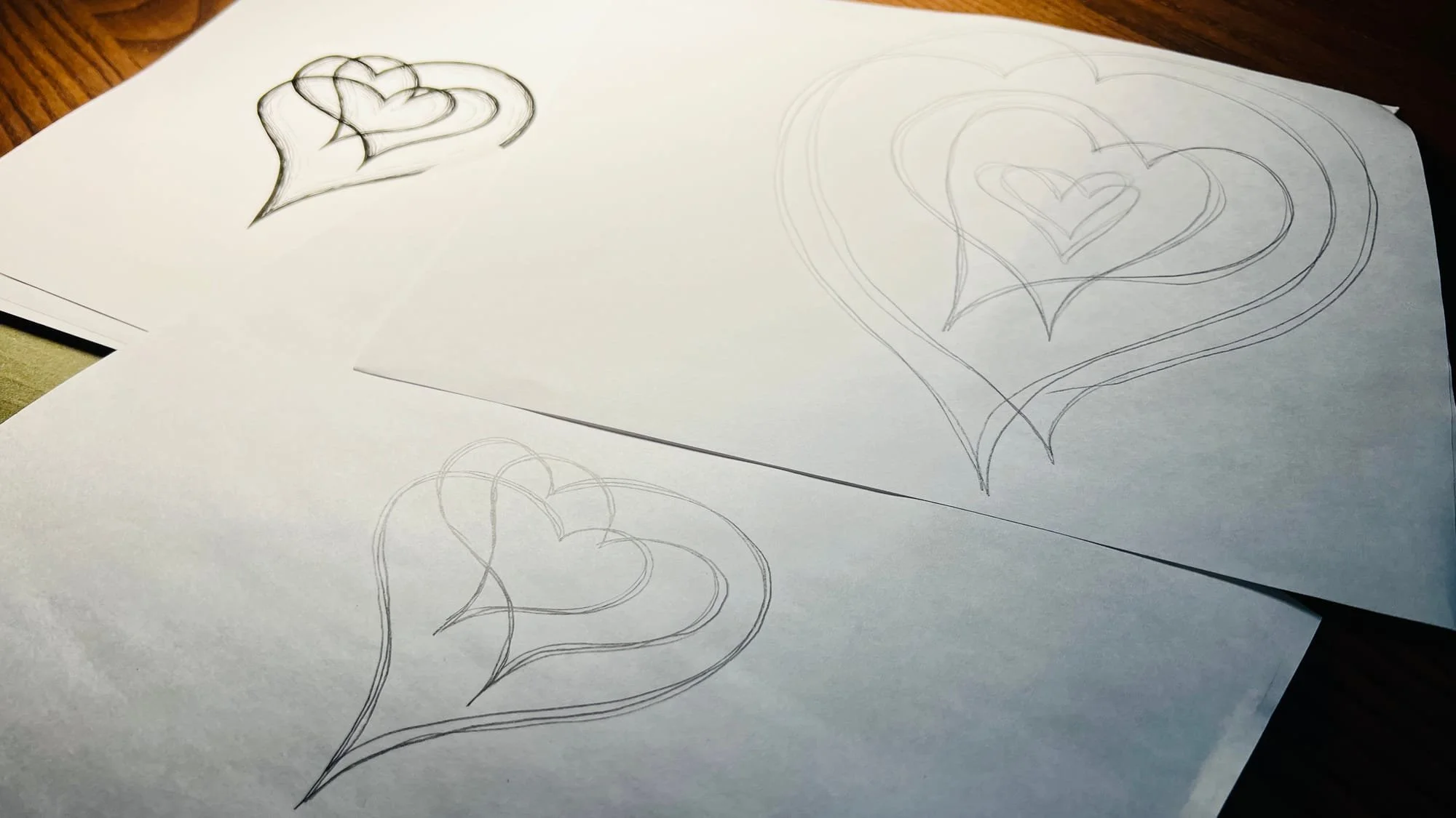 Pencil sketch iterations of layered heart design on white paper, showing design exploration and creative process for children's book illustration