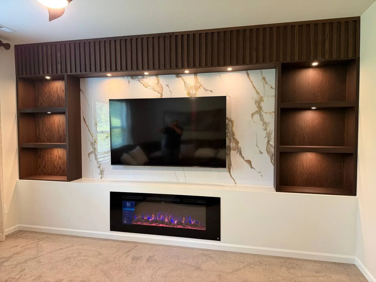 Custom TV media wall with electric fireplace, marble surround and walnut slat shelving — finished installation in Charlotte, NC