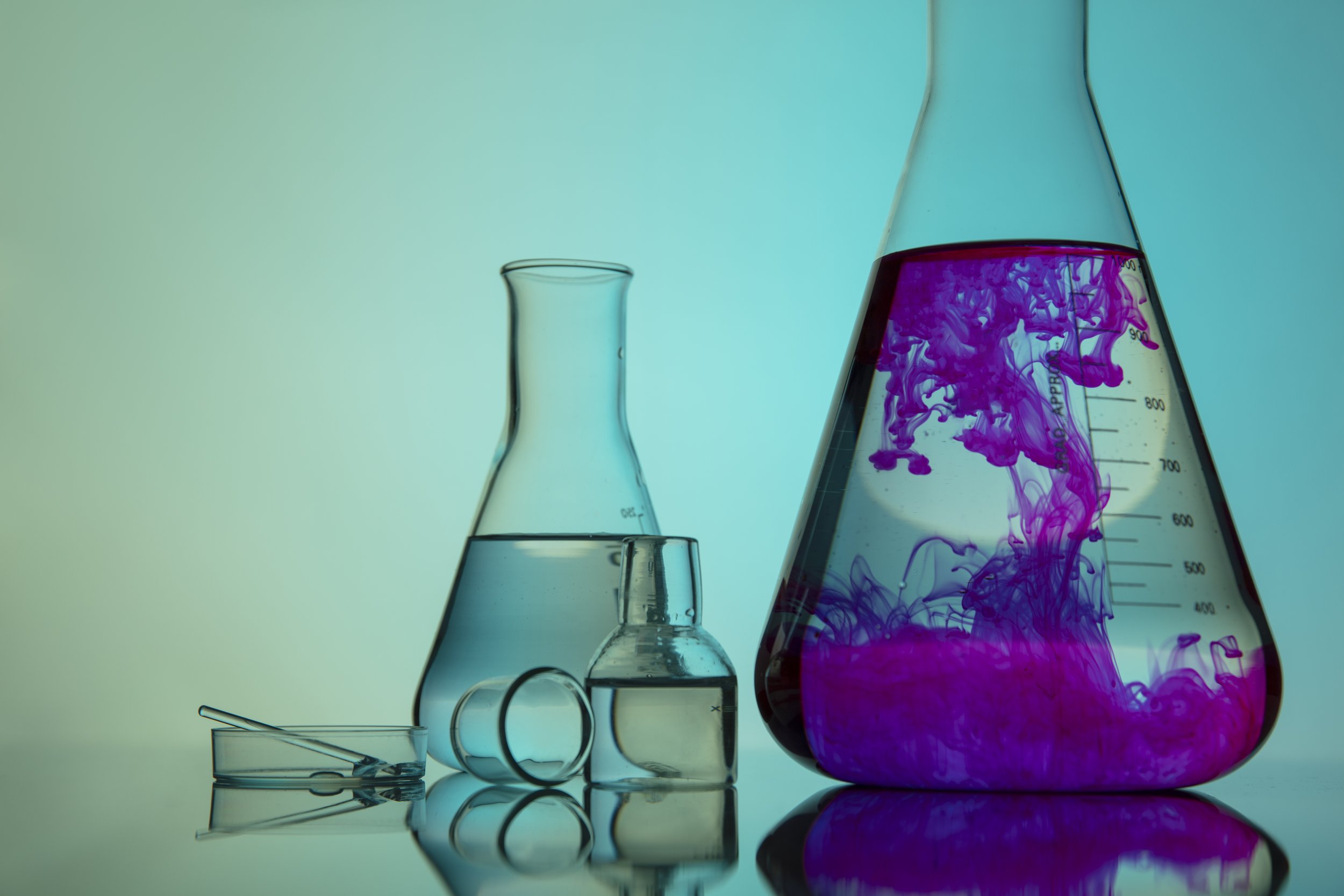 glass beakers on a table, with larger beaker filled with pink solution