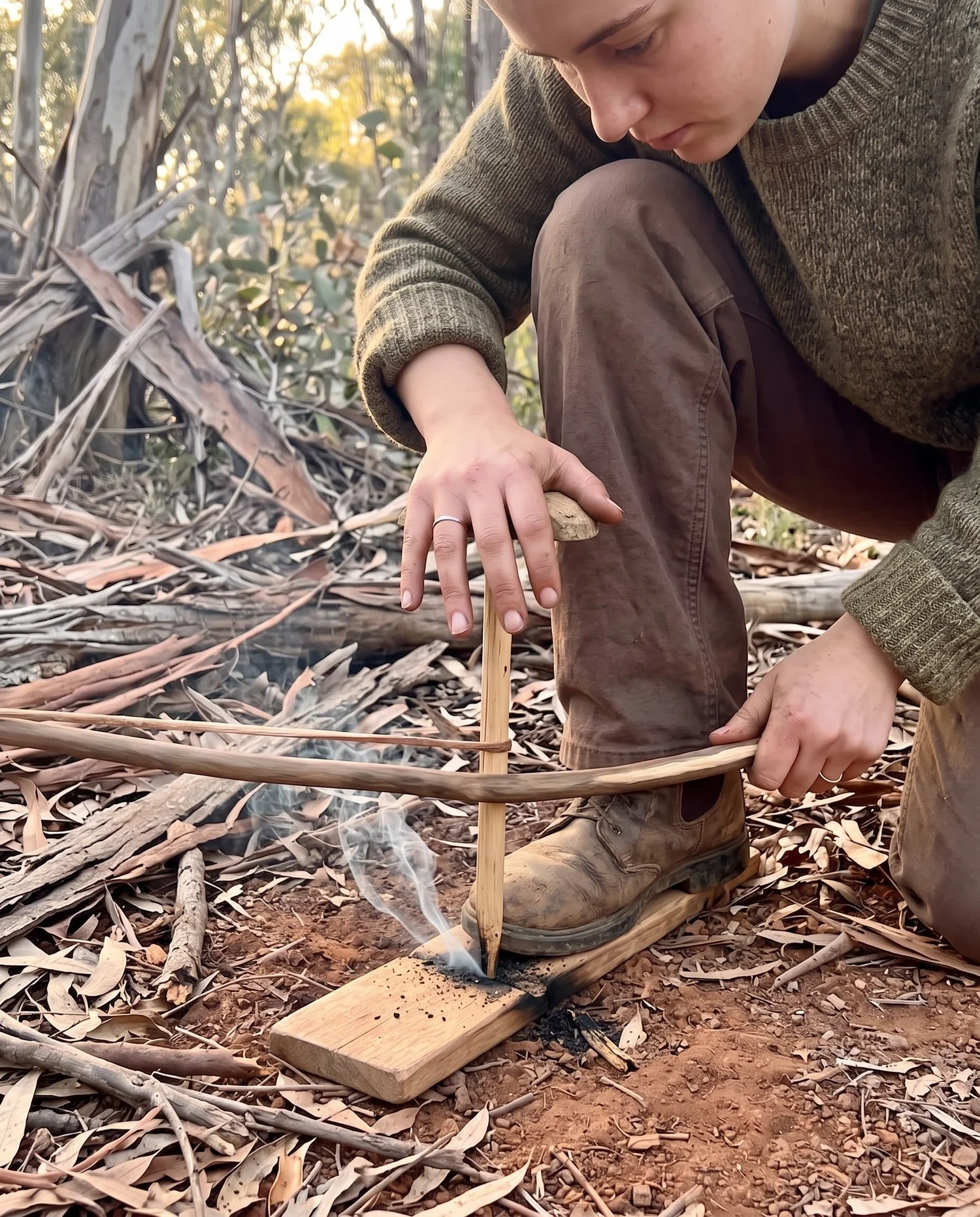 Hands working a bow drill to create an ember