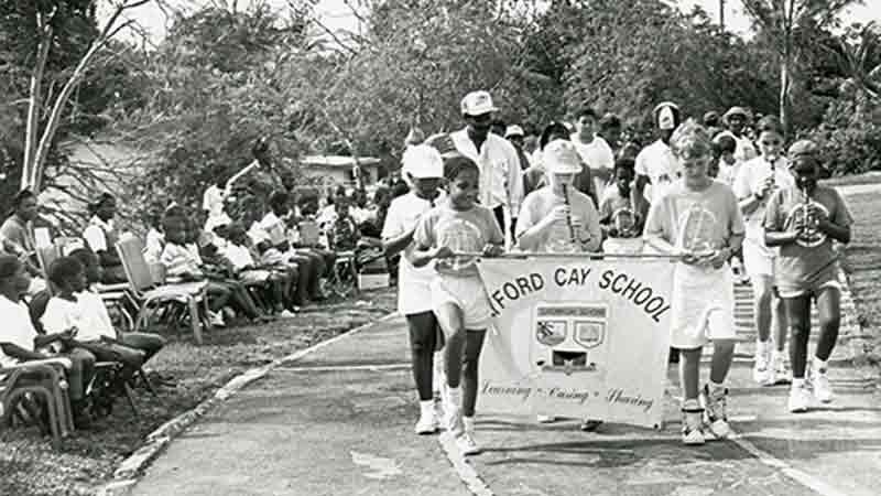 Black and white photo of students holding school banner marching in parade.