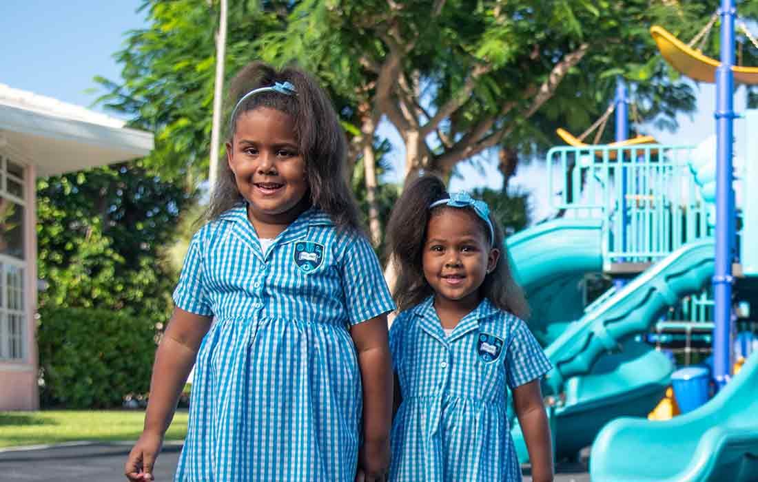 Two young students in blue and white check school dress uniforms on playground.