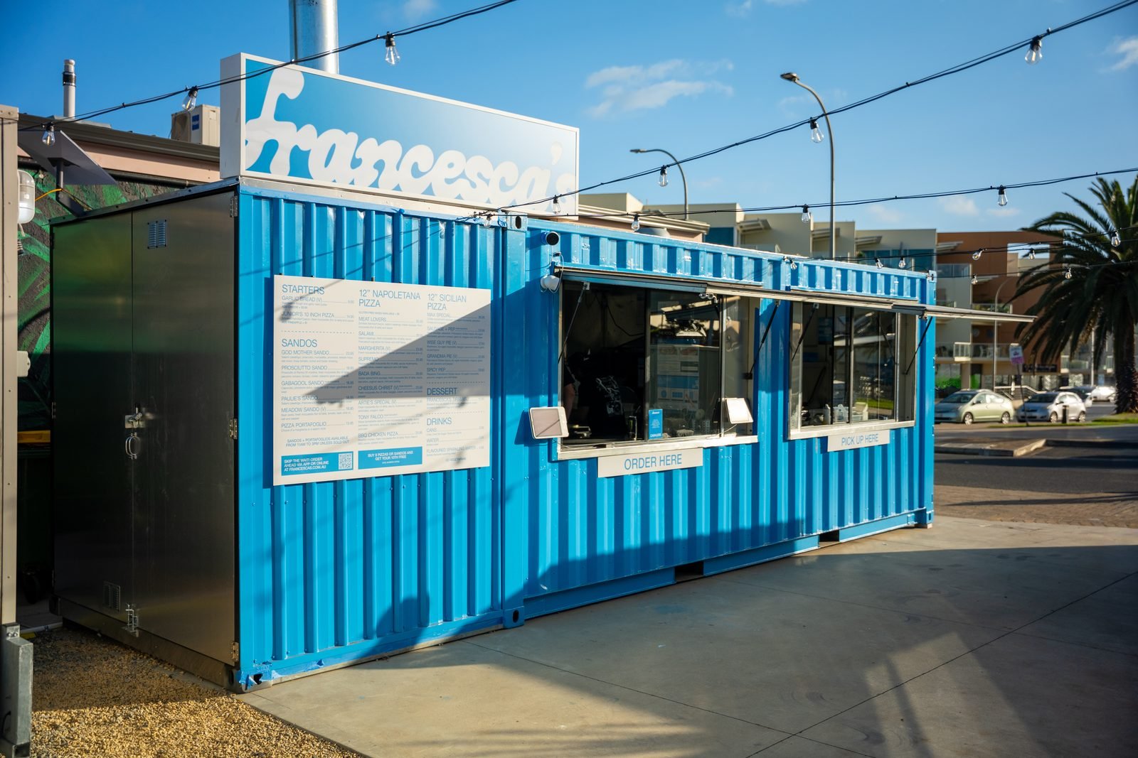 The Francesca’s Pizza + Sandos shipping container at 13 Beach Road, Christies Beach, painted blue with the wordmark on top and the menu board on the side
