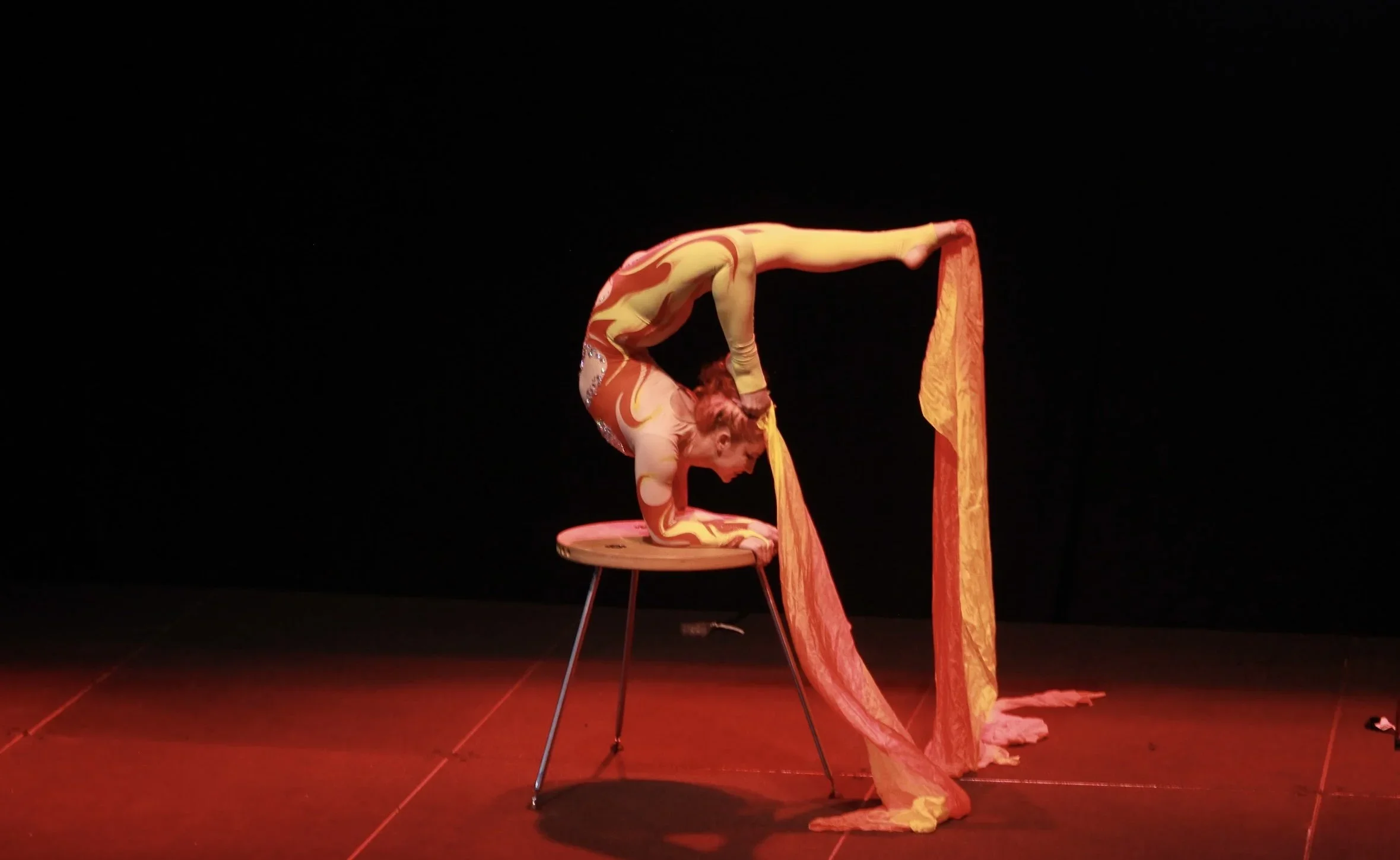Talia Hazard holding an inverted backbend on a stand with peach-colored fabric
