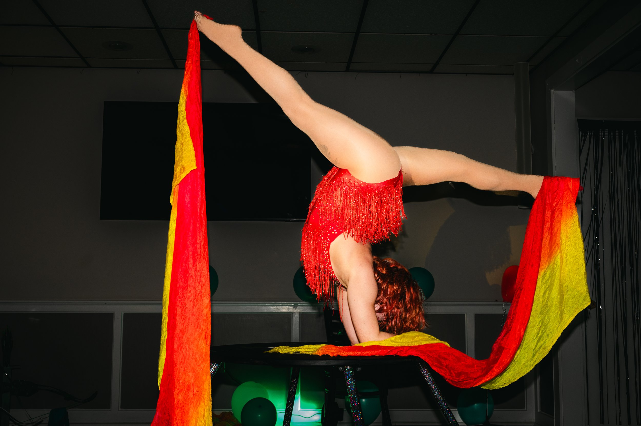 Talia Hazard balancing upside down in a red costume with flowing rainbow fabric