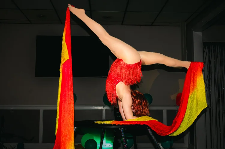 Talia Hazard balancing upside down in a red costume with flowing rainbow fabric