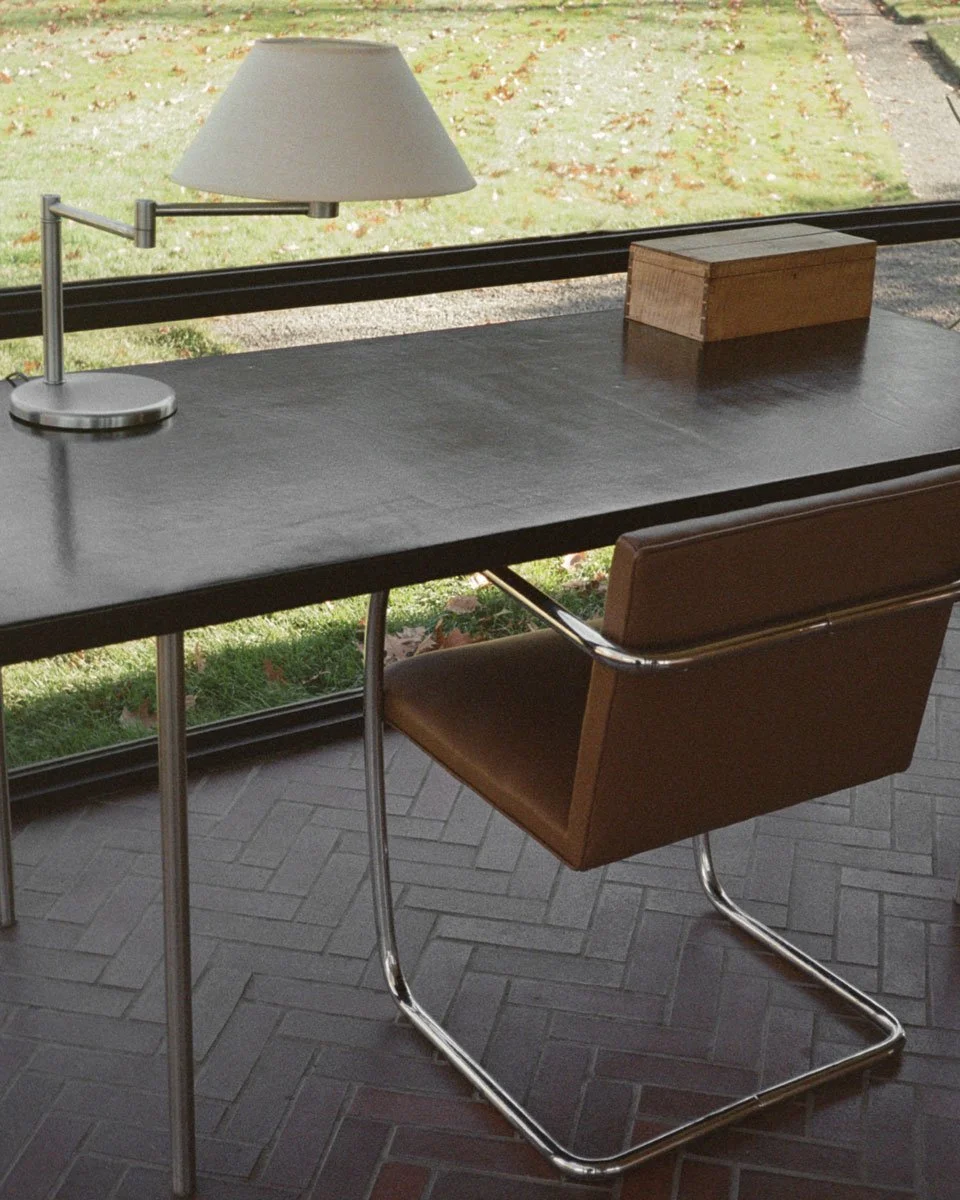 A modern desk with a lamp, wooden box, and brown leather chair.